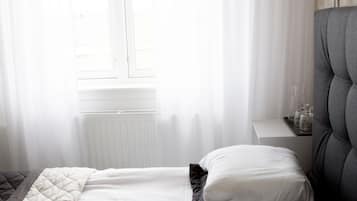 A bedroom with a bed, white curtains, a bedside lamp, and a radiator.