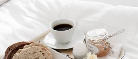 A breakfast tray with bread, cheese, ham, and eggs on a bed with white linens.