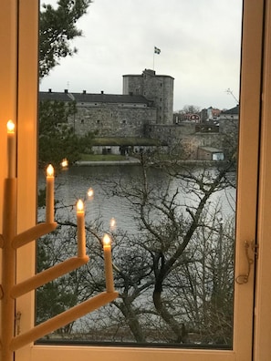 A view of a stone castle with a flag, a body of water, and bare trees. - Sjövillan (Vaxholm)