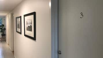 A hallway with two framed pictures on the wall, a door with the number 3, and a potted plant in the corner.
