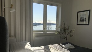 A hotel room with a bed, a window with a view of a lake, a radiator, and a wall-mounted picture.