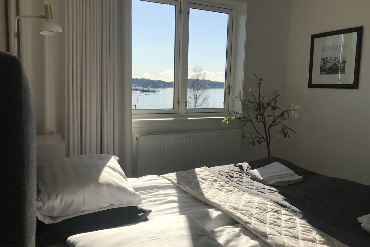 Ein Hotelzimmer mit Bett, Fenster mit Seeblick, Heizkörper und einem Wandbild.