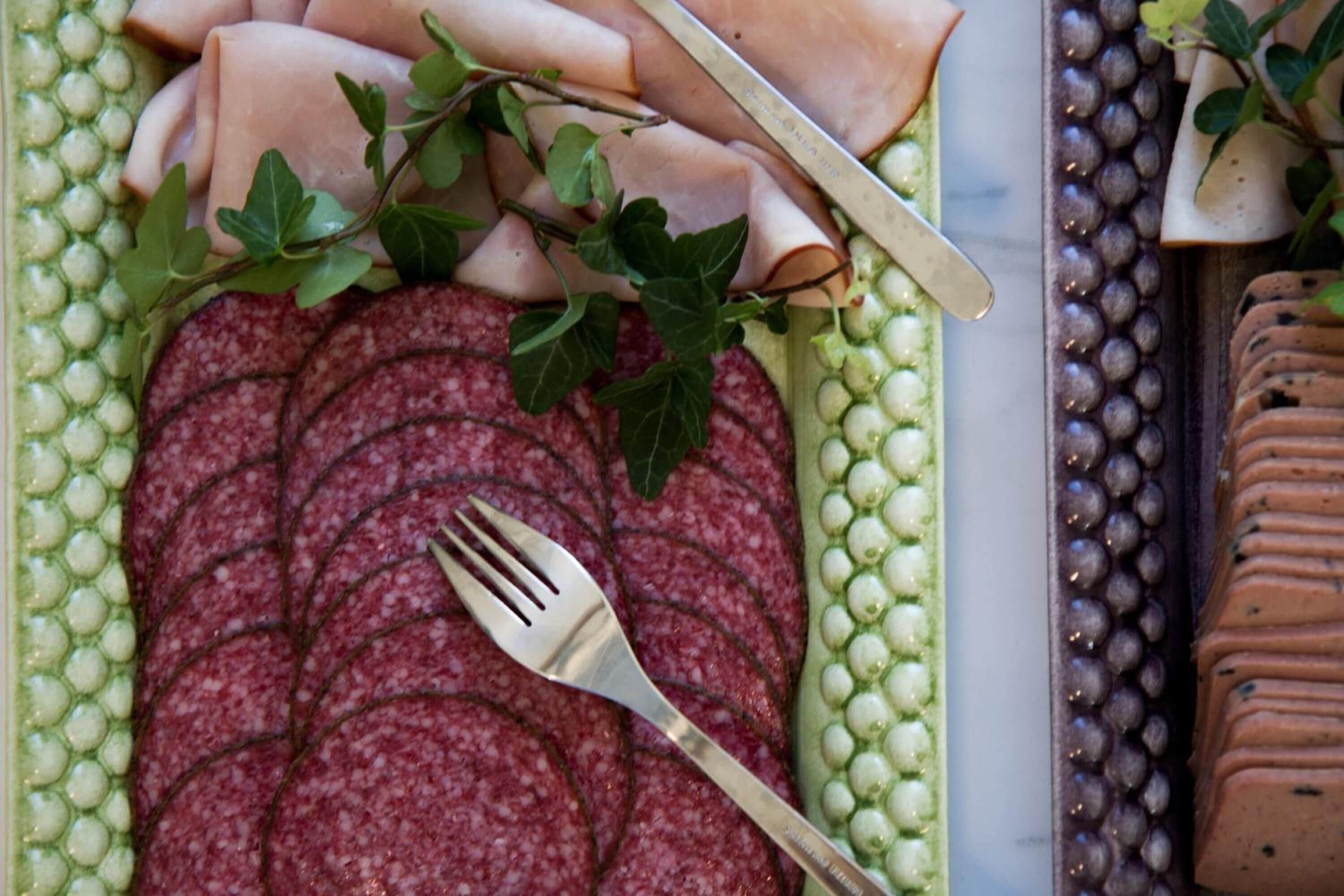 Un piatto di salumi affettati e una forchetta su un piatto decorativo.