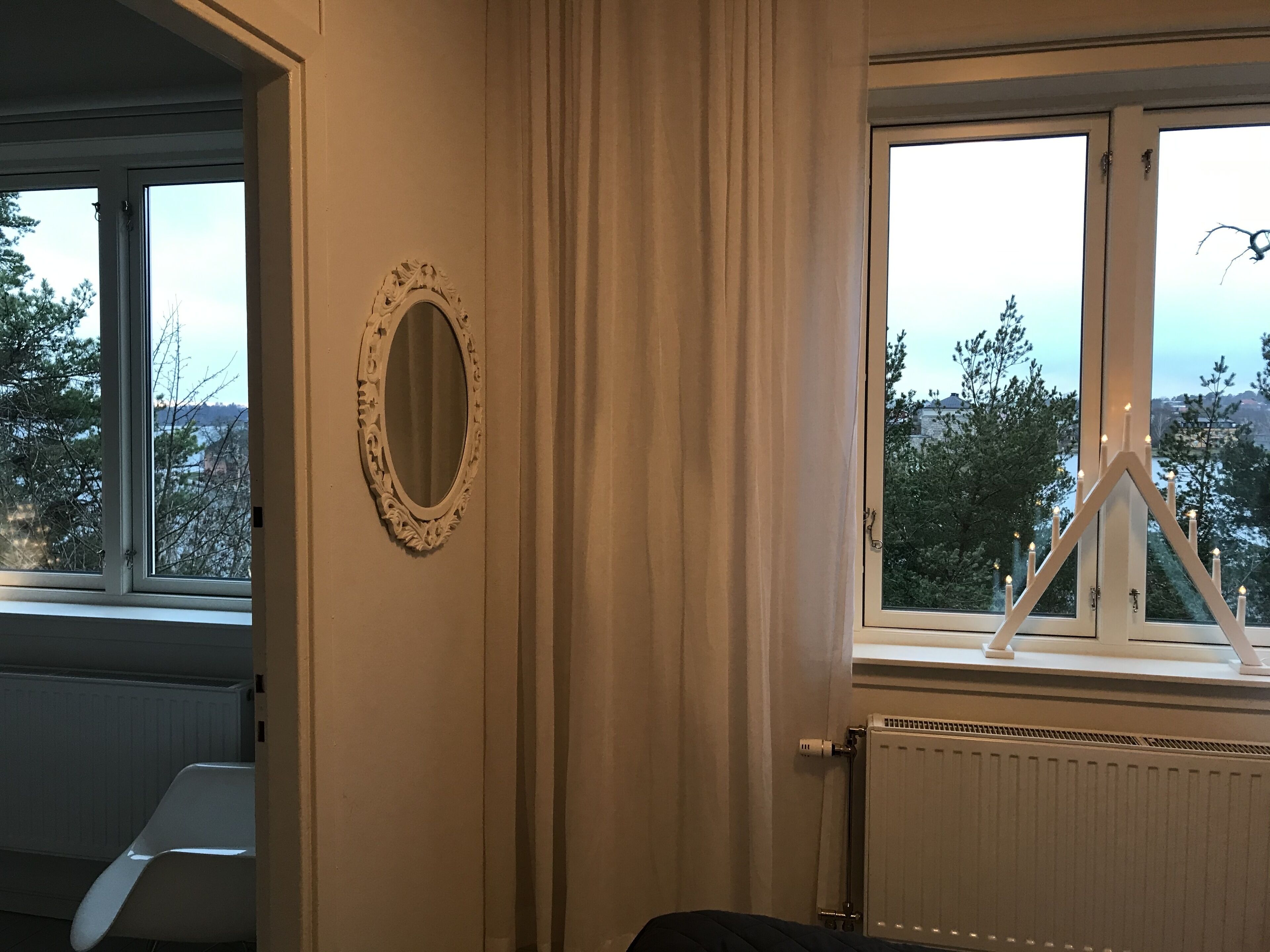 Ein Zimmer mit einem großen Fenster, einem Heizkörper, einem Stuhl und einem Spiegel an der Wand.