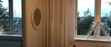 A room with a large window, a radiator, a chair, and a mirror on the wall.