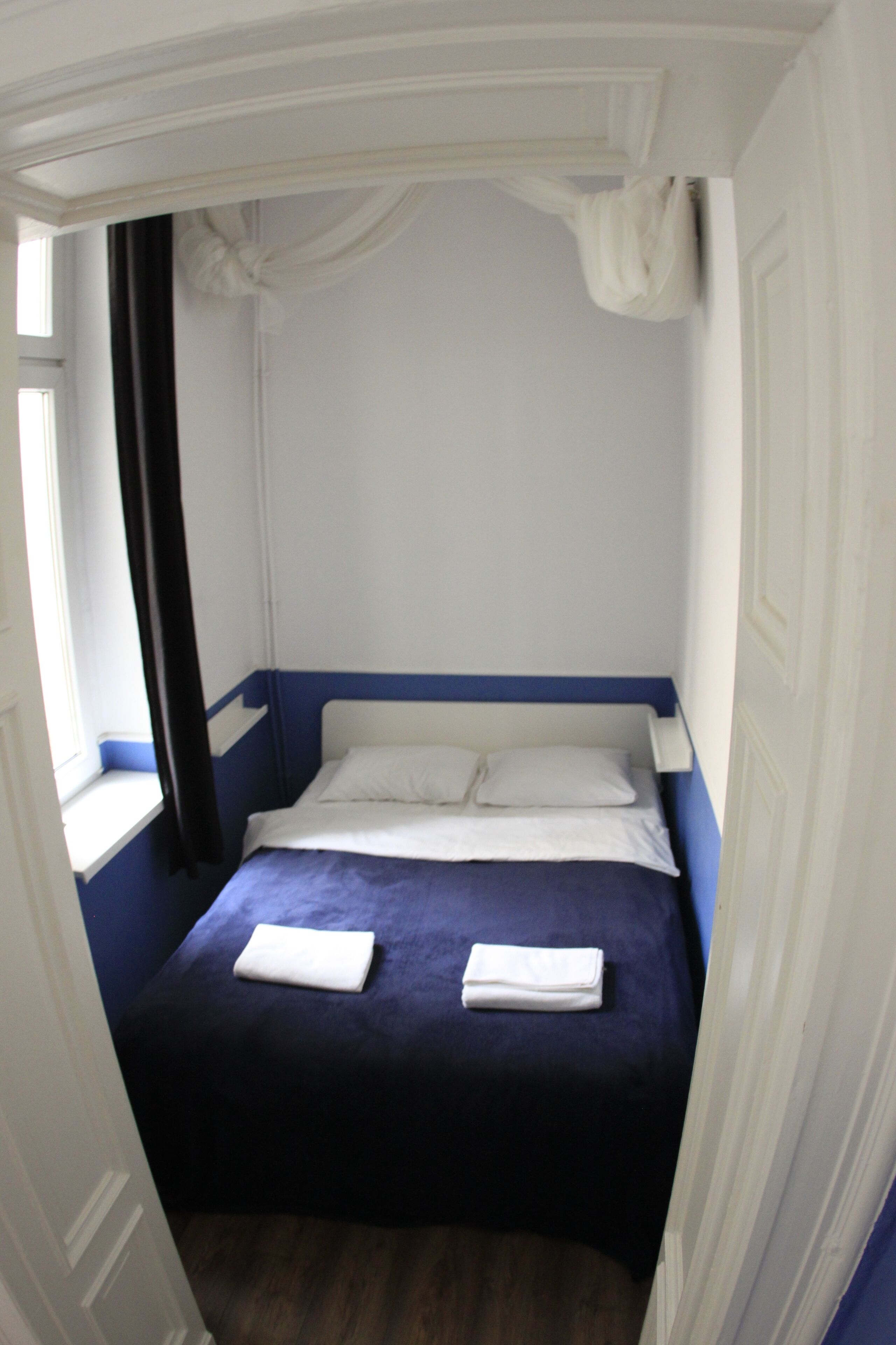 Une pièce avec un lit, des rideaux blancs et une fenêtre.