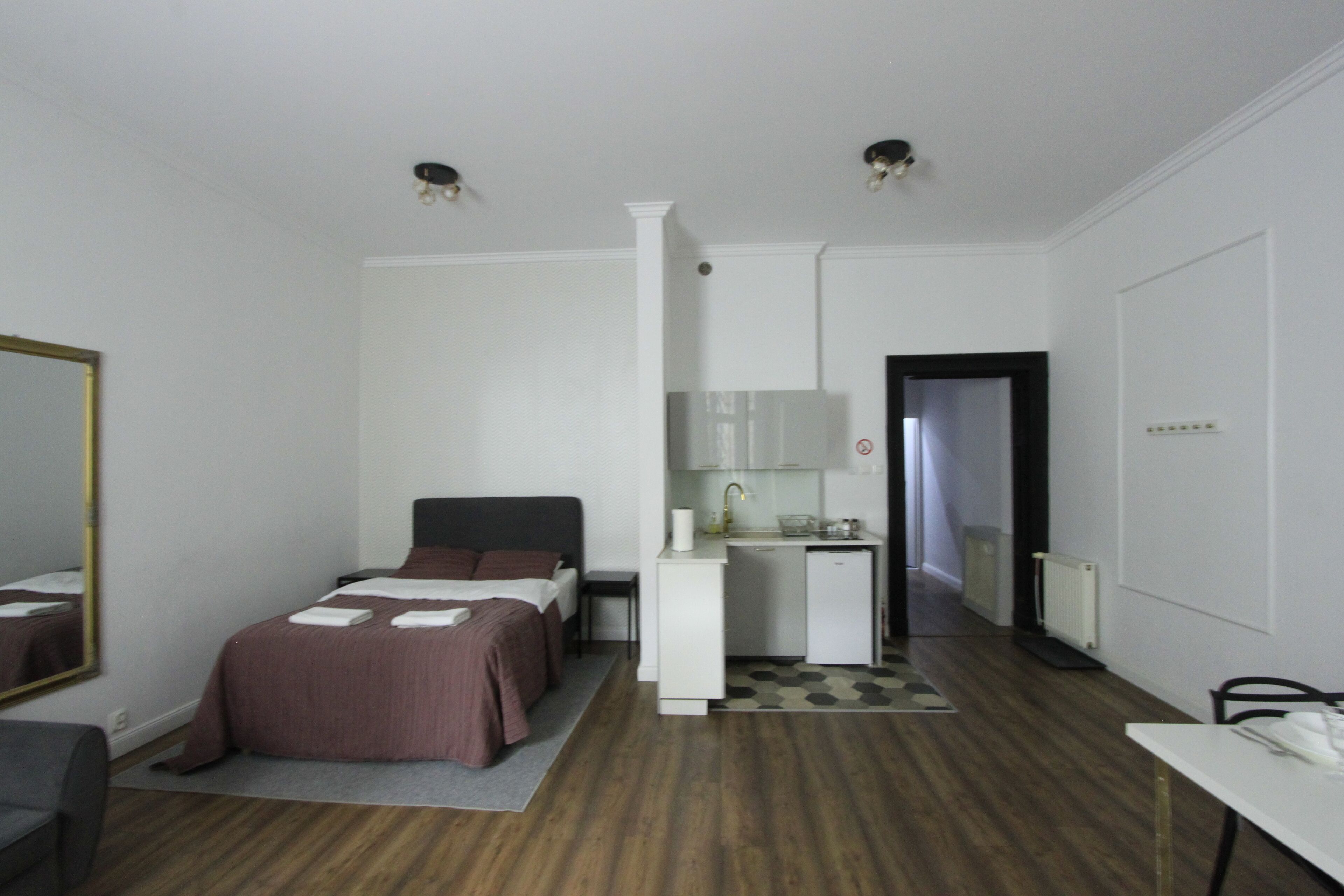 Habitación de hotel pequeña con cama, escritorio, espejo y una kitchenette.