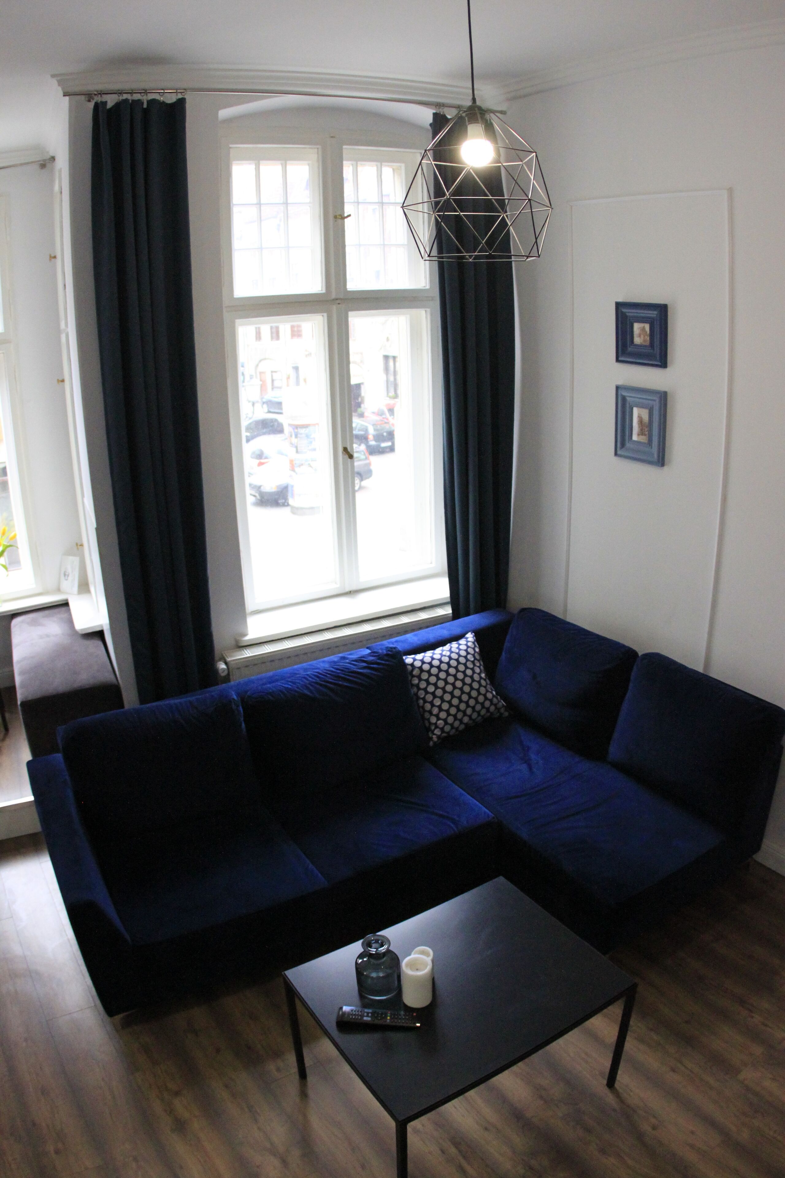 Un salon moderne avec un canapé bleu foncé, une petite table basse noire et un luminaire suspendu aux motifs géométriques.