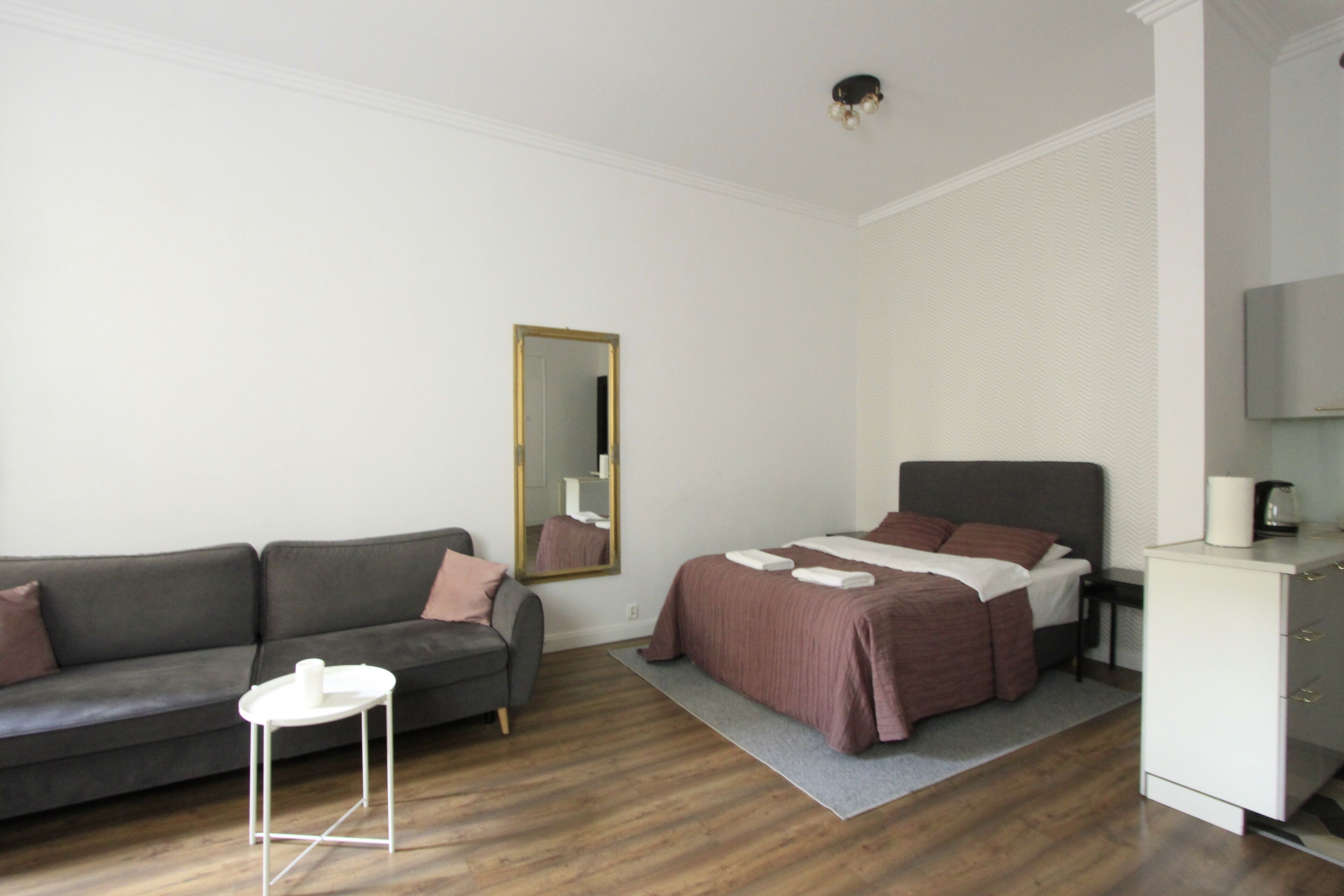 A modern bedroom with a bed, a sofa, a small table, and a mirror.