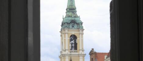Vista a través de una ventana de un edificio con una torre de reloj y una estatua al frente.