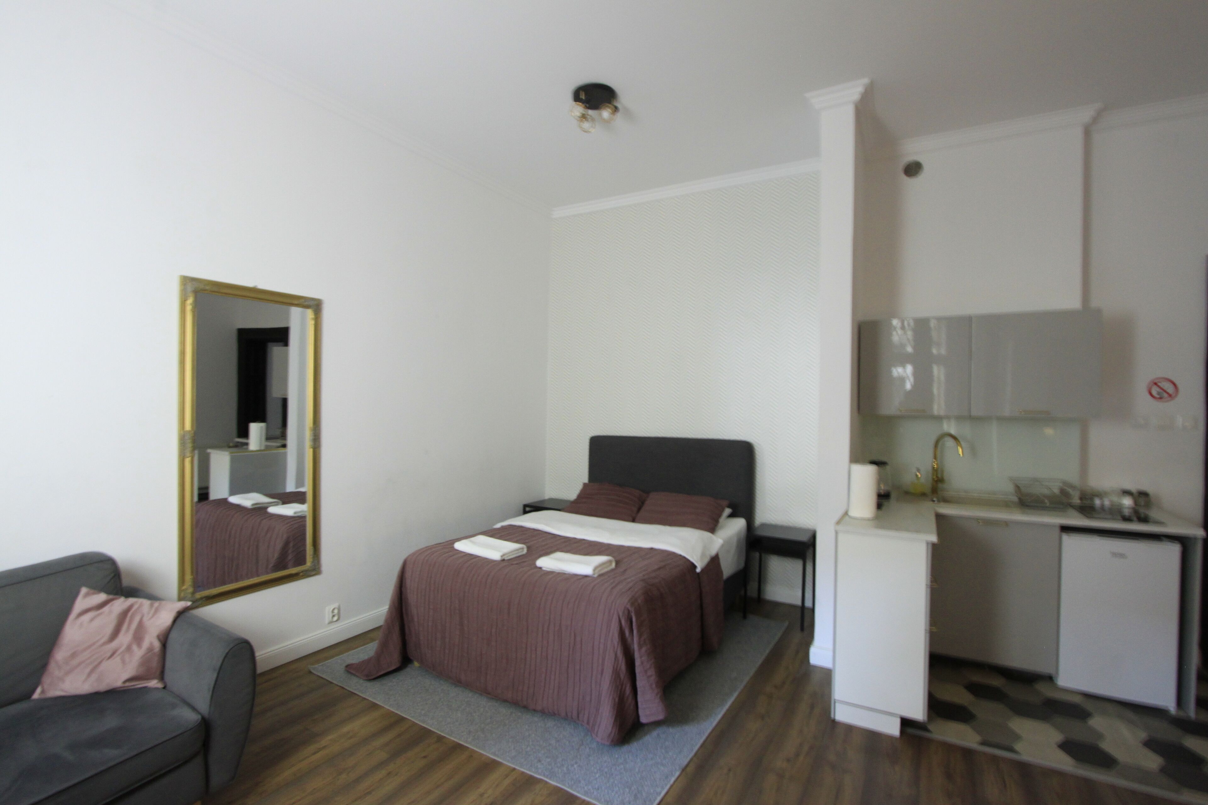 A modern hotel room with a bed, bedside table, and a small kitchenette.