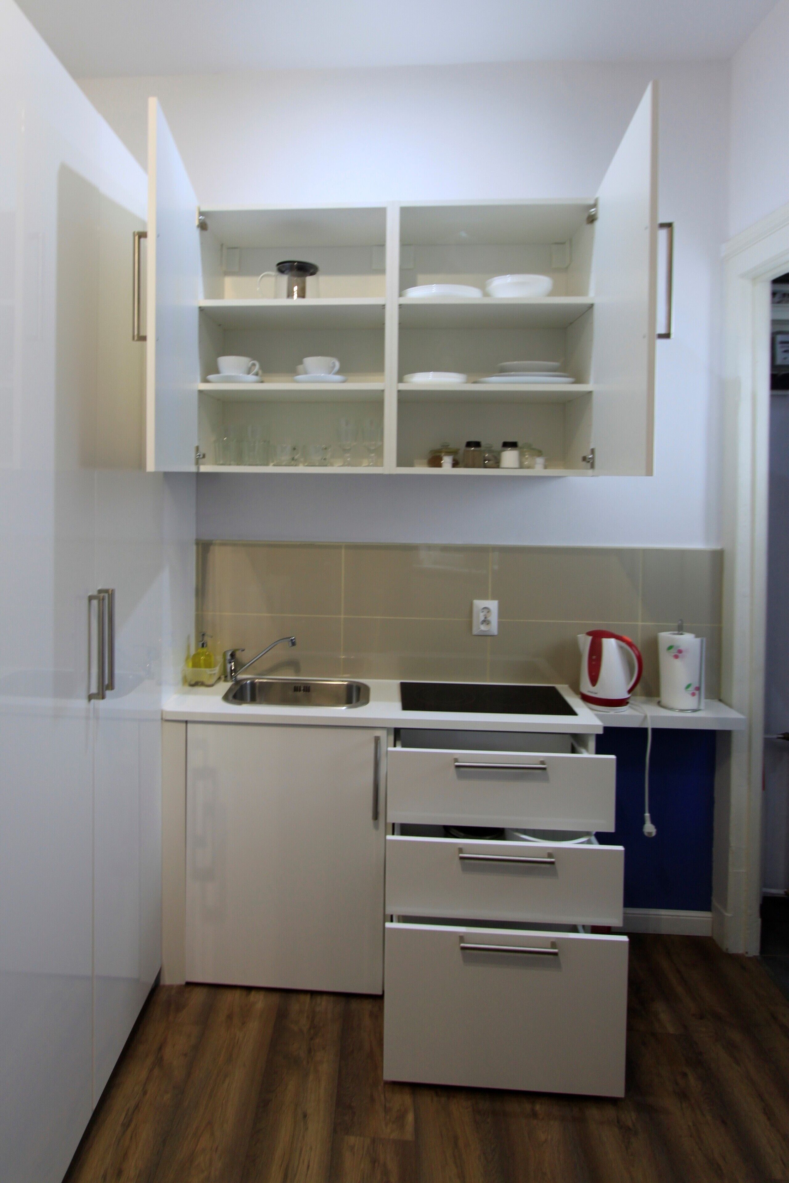 A compact kitchen with white cabinetry, a sink, and a kettle.