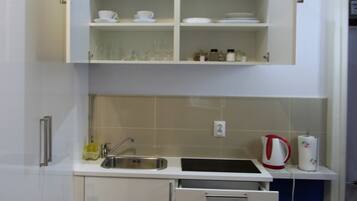A compact kitchen with white cabinetry, a sink, and a kettle.