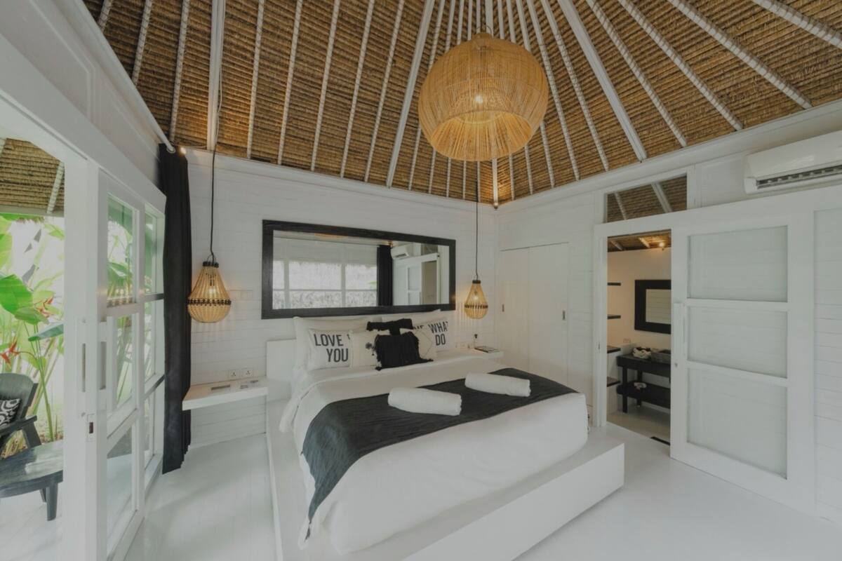 Une chambre à coucher avec un lit, un grand miroir, un ventilateur de plafond et une vue sur la salle de bain.