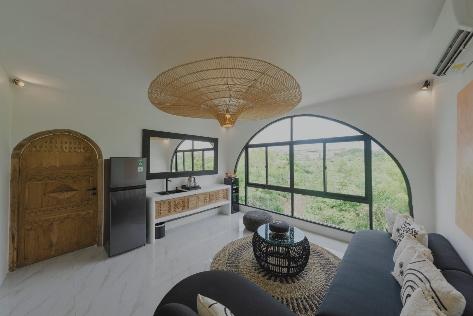 A modern kitchen with a large window, a wooden door, and a black sofa with a woven rug.