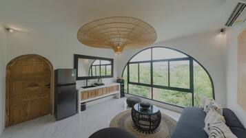A modern kitchen with a large window, a wooden door, and a black sofa with a woven rug.