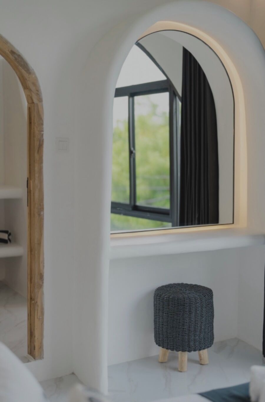 A bathroom with a white vanity, a small stool, and a window with a view of greenery.