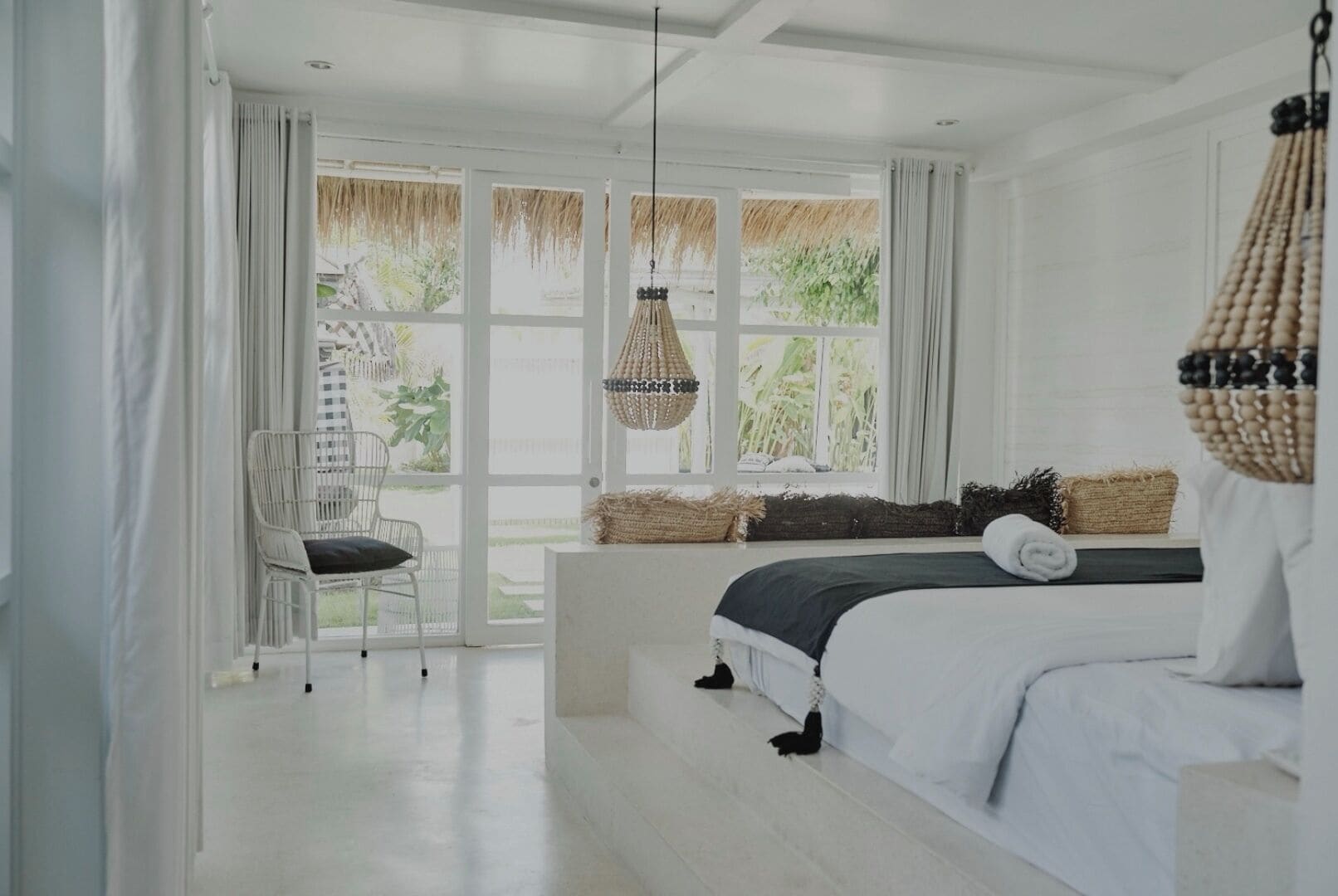 A bedroom with a bed, a chair, a hanging light, and a view of greenery outside.
