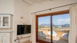 Habitación con televisor, mueble y puerta corrediza de vidrio que da a una zona de estar exterior con vistas del paisaje.