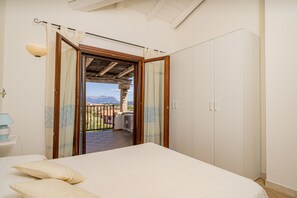 A bedroom with a bed, a nightstand, and a view of a balcony with a mountain backdrop. - Casa Lola (Olbia)