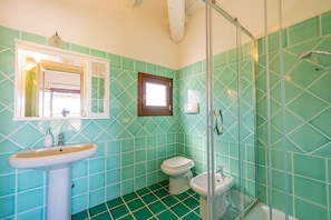 A bathroom with a sink, toilet, and shower area, featuring green tiles and a window. - Casa Lola (Olbia)
