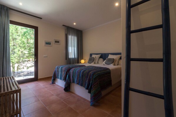Un dormitorio con cama, ventana, puerta y vistas a árboles fuera.