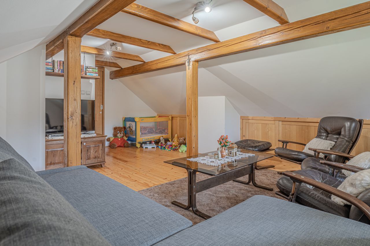 A loft-style room with exposed wooden beams, a glass coffee table, leather recliner, and a bookshelf.