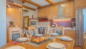 A dining area with a wooden table set for six, surrounded by wooden cabinets and a stainless steel refrigerator. - Vineyard Cottage Stepan (Crnomelj)
