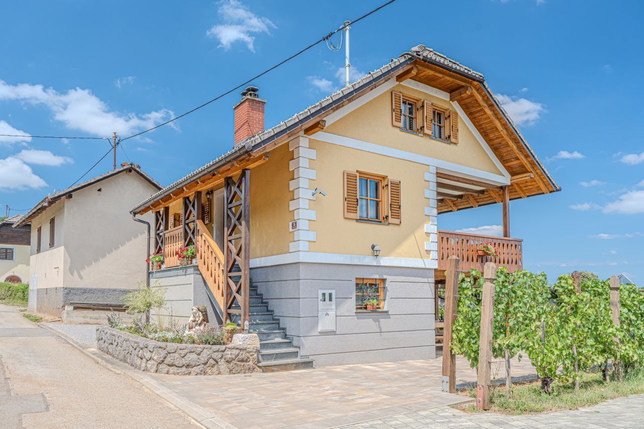 Une maison à deux étages avec un escalier en bois, un balcon et un mur en pierre.