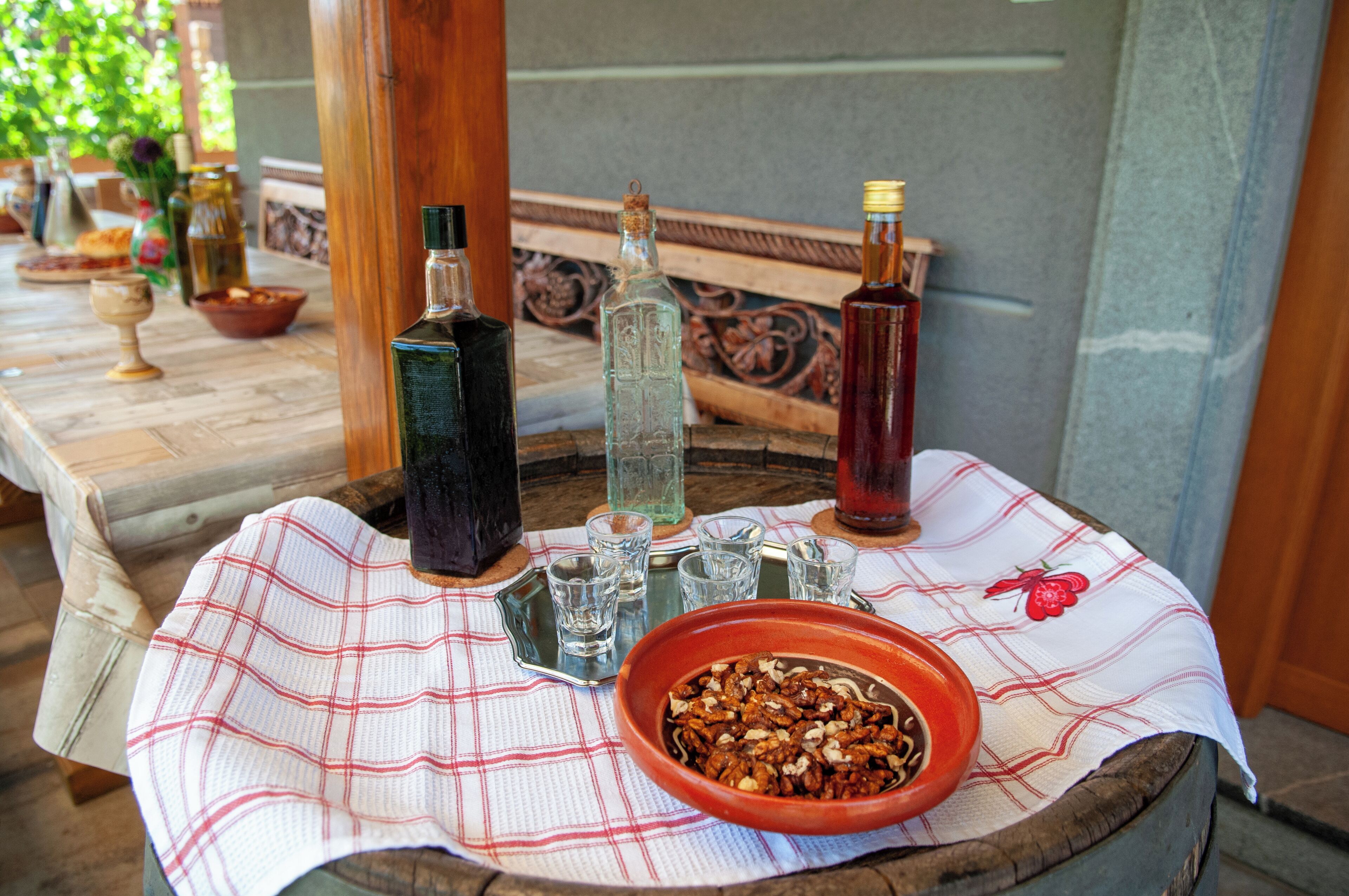 A table with a checkered tablecloth, a bowl of nuts, and three bottles.