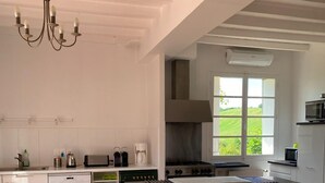 Une cuisine avec des meubles blancs, un îlot central doté d’un plan de travail noir, une cuisinière et une fenêtre donnant sur un paysage verdoyant.