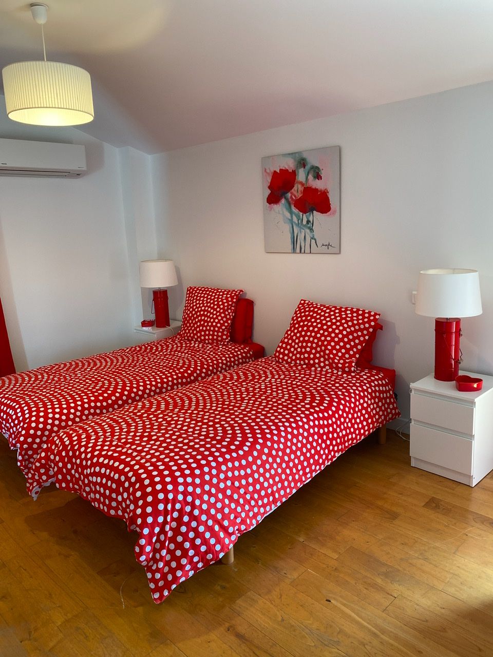 Une chambre à coucher avec un lit recouvert d’une couette à pois rouges, deux tables de chevet avec des lampes et un tableau accroché au mur.