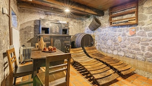 A rustic dining area with a stone wall, wooden table, chairs, and a barrel. - Vineyard Cottage Škatlar 1 (Novo Mesto)