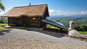 A rustic wooden cabin with a thatched roof, a stone chimney, and a gravel driveway. - Vineyard Cottage Škatlar 1 (Novo Mesto)