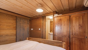 A wooden-paneled room with a bed, a wooden wardrobe, and a bathroom visible through an open door. - Vineyard Cottage Škatlar 1 (Novo Mesto)
