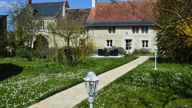 A stone building with a red-tiled roof, a paved pathway, and a garden with white flowers. - La Balastière (Beaumont-en-Veron)
