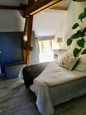 A bedroom with a bed, a nightstand, a lamp, a plant, and a view of the outdoors. - La Balastière (Beaumont-en-Veron)