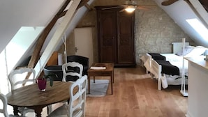 A cozy attic room with a sloped ceiling, wooden beams, a bed, a desk, and a dining table with chairs. - La Balastière (Beaumont-en-Veron)