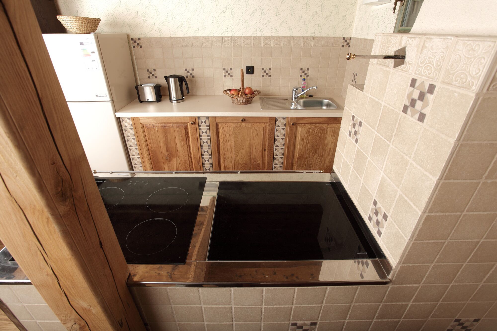 Una cocina compacta con armarios de madera, una placa de inducción negra, un horno empotrado, un lavamanos pequeño y un tostador.