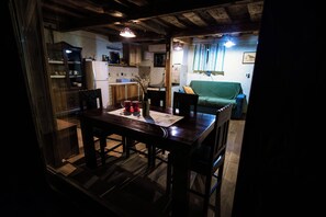A dimly lit room with a wooden table, chairs, a sofa, and a kitchen area in the background. - Vineyard cottage Škatlar 2 (Novo Mesto)