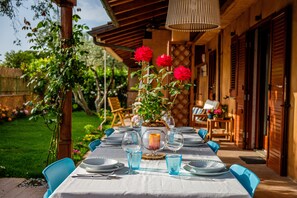 A dining table set outdoors with blue chairs, a candle centerpiece, and a potted plant with red flowers. - Elegant villa with a private pool in Capalbio Scalo (Capalbio Scalo)