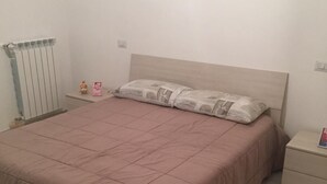 Une chambre à coucher comprenant un lit, une table de chevet, un radiateur et une prise électrique murale.