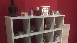 Une bibliothèque blanche se dresse contre un mur rouge, et est remplie de divers objets, notamment des livres, des figurines et des objets décoratifs.