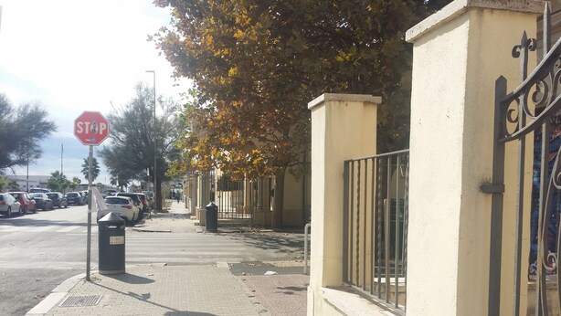 Un trottoir avec un panneau de signalisation indiquant un arrêt obligatoire, une poubelle et une entrée fermée par un portail et une clôture en métal.