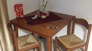 Une petite table à manger avec deux chaises en bois, un vase avec des fleurs, une télécommande et un paquet de collations.