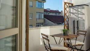 A balcony with a table and chairs, a potted plant, and a view of neighboring buildings.
