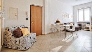 A living room with a sofa, a dining table with chairs, a wooden door, and framed pictures on the wall.