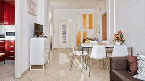 A modern living room with a dining area, white walls, and a kitchen with red cabinets.