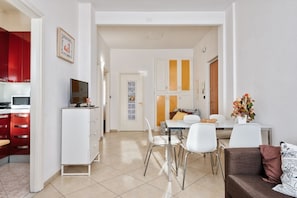 A modern living room with a dining area, white walls, and a kitchen with red cabinets.