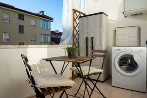 A balcony with a washing machine, a table, and two chairs.